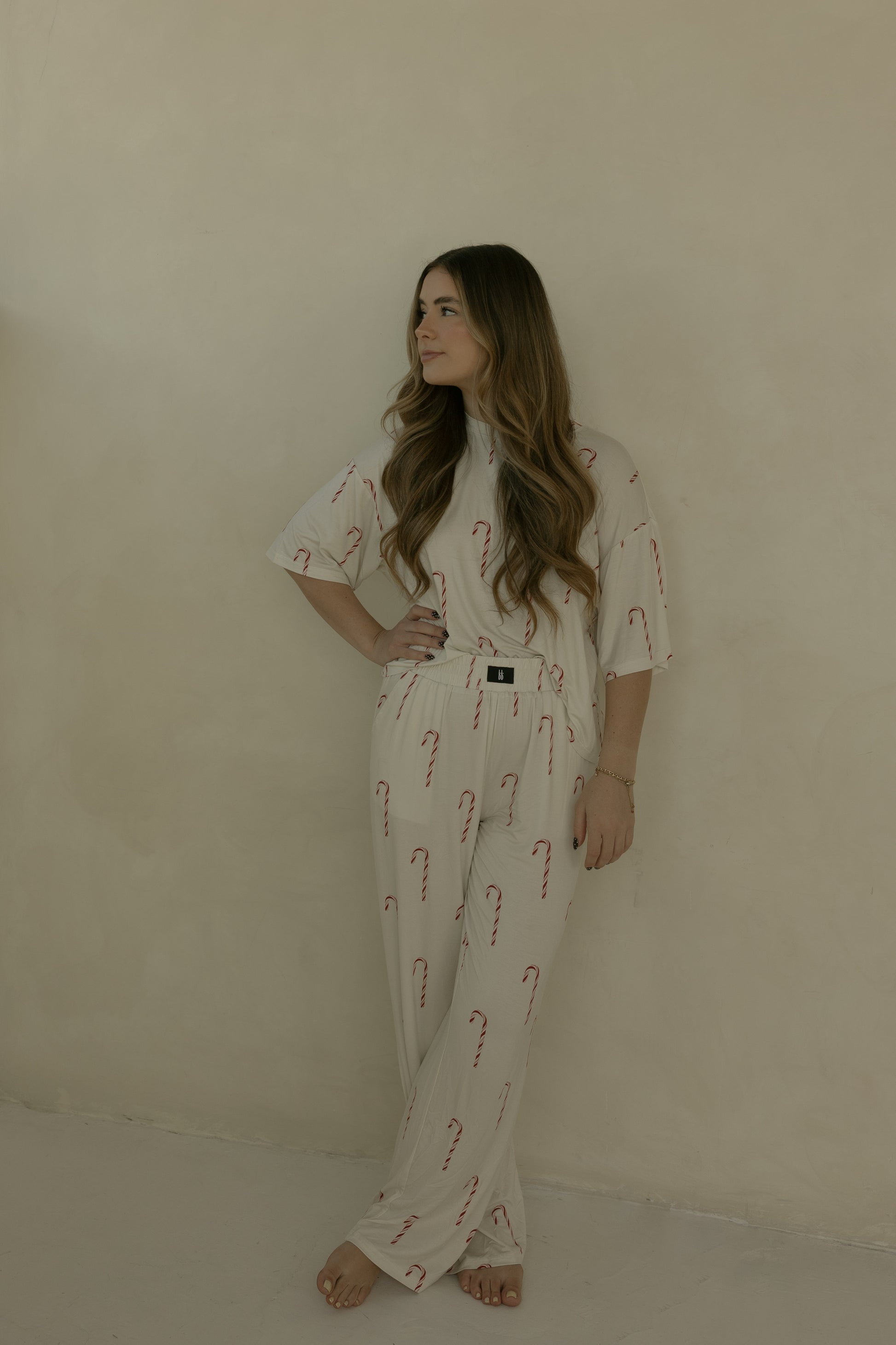 A woman with long hair stands barefoot against a beige wall, wearing the forever french baby Women's Boxy Tee Lounge Set in Candy Cane—an ultra-soft, hypoallergenic bamboo outfit perfect for lounging or sleep. She has one hand on her hip and looks to the side.