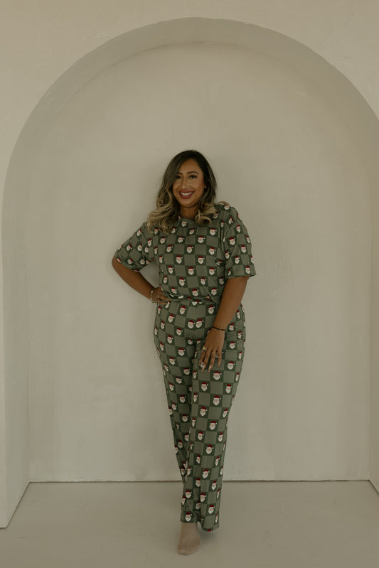 A woman with shoulder-length hair smiles under a white arch, wearing the forever french baby Women's Boxy Tee Lounge Set in Santa Checkerboard. She stands with one hand on her hip against a plain, neutral background.