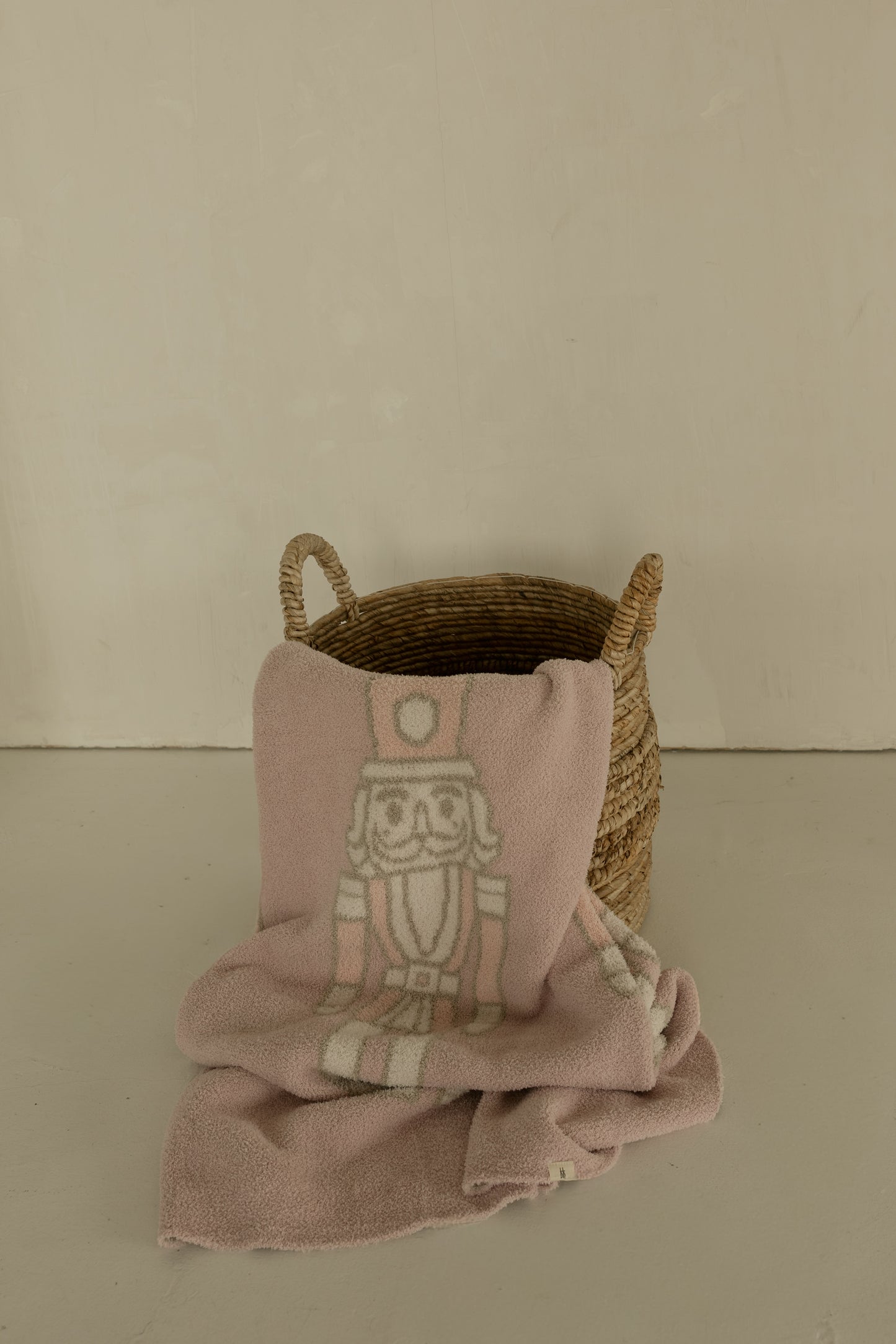 The forever french baby Plush Blanket | Nutcracker, with a white nutcracker outline, is draped over a woven basket on a light floor against a plain beige wall.