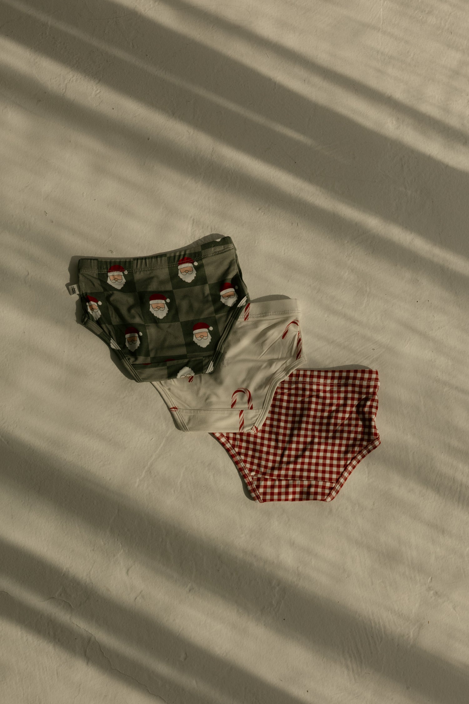 The forever french baby Girl's Bamboo Briefs (3 Pack) features red gingham, candy cane, and Santa checkerboard prints. Made from hypoallergenic bamboo for comfort and style, these briefs are beautifully displayed on a light surface with soft shadows.