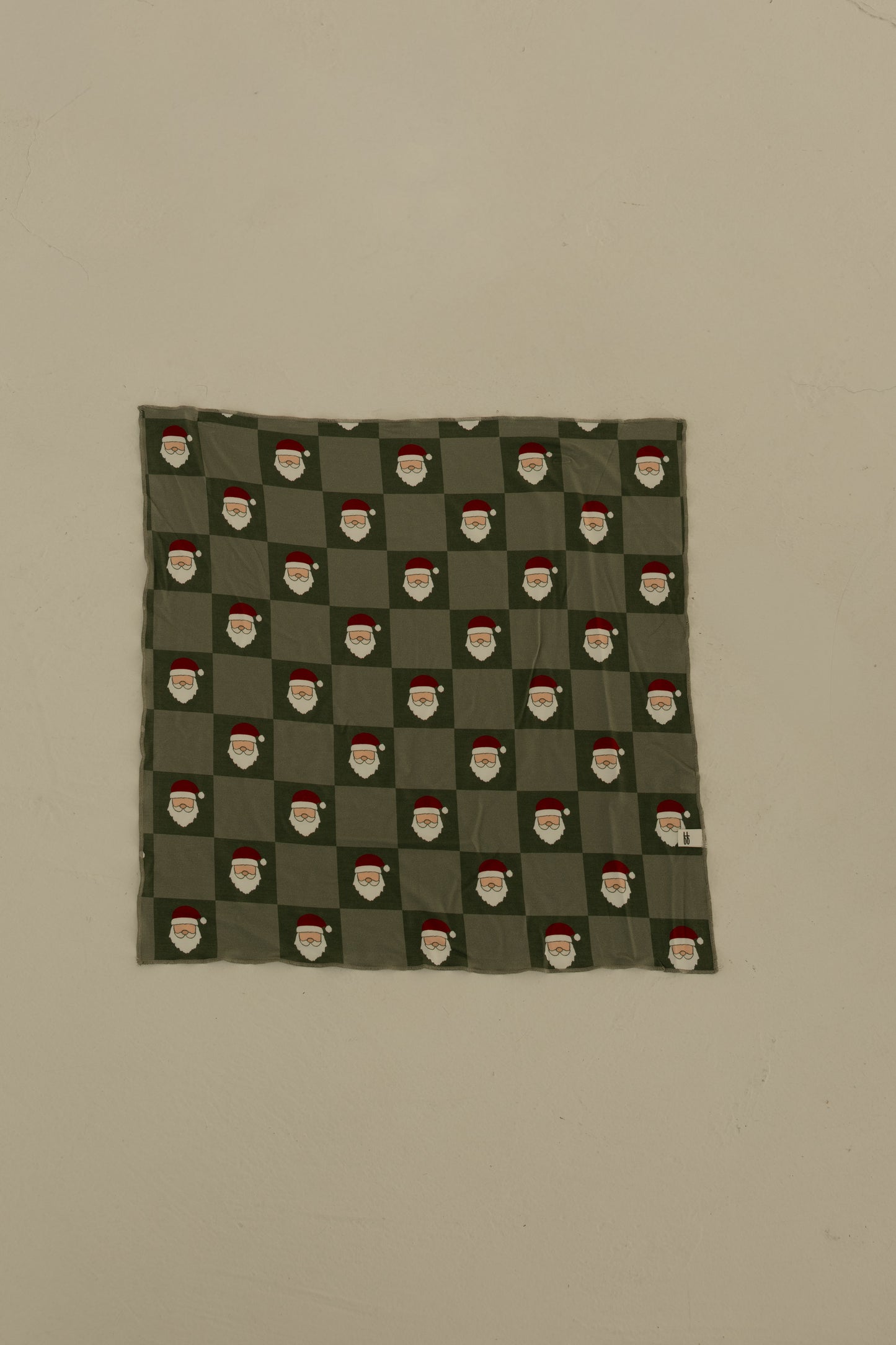 The Bamboo Bandana | Santa Checkerboard by forever french baby is a green, soft bamboo viscose pet bandana with a repeating Santa checkerboard pattern, shown pinned flat to a plain beige wall.