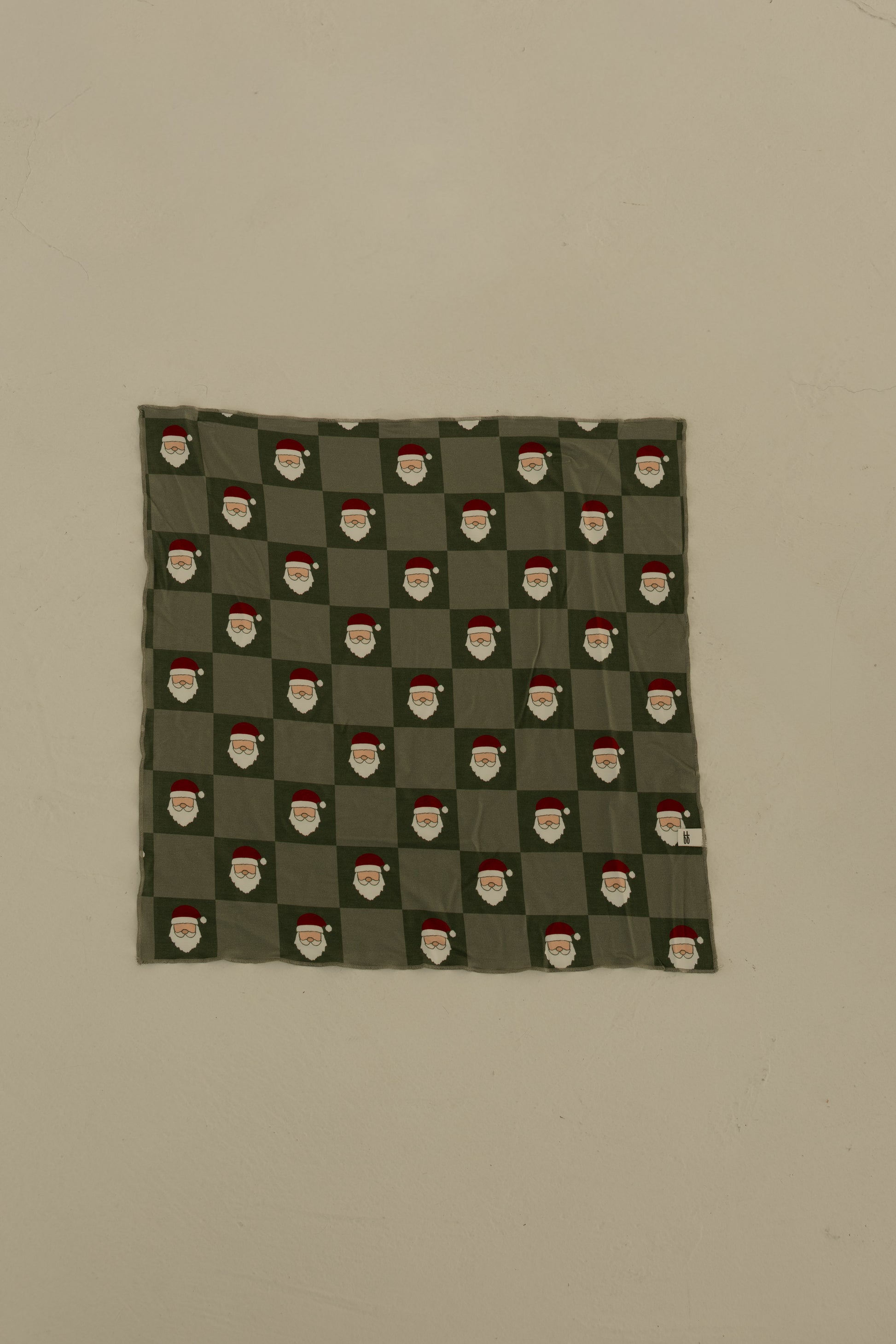 The Bamboo Bandana | Santa Checkerboard by forever french baby is a green, soft bamboo viscose pet bandana with a repeating Santa checkerboard pattern, shown pinned flat to a plain beige wall.