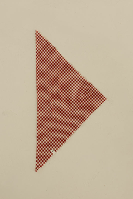 The Bamboo Bandana | Red Gingham by forever french baby, cut in a right triangle shape, is displayed on a plain beige surface.