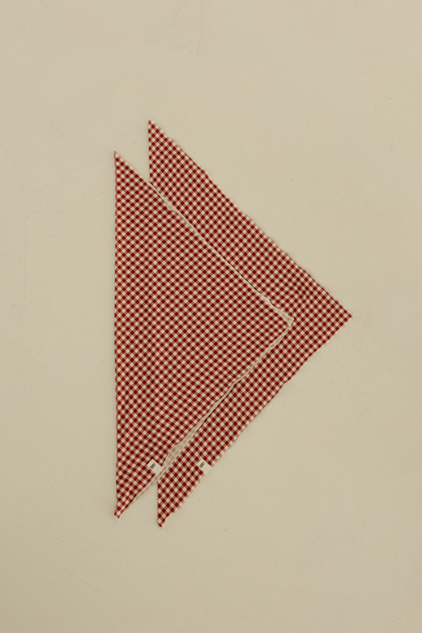 Two Bamboo Bandana | Red Gingham pieces from forever french baby, featuring a red and white checkered pattern, are stacked on a light beige surface with playful overlap, resembling classic bandana style.