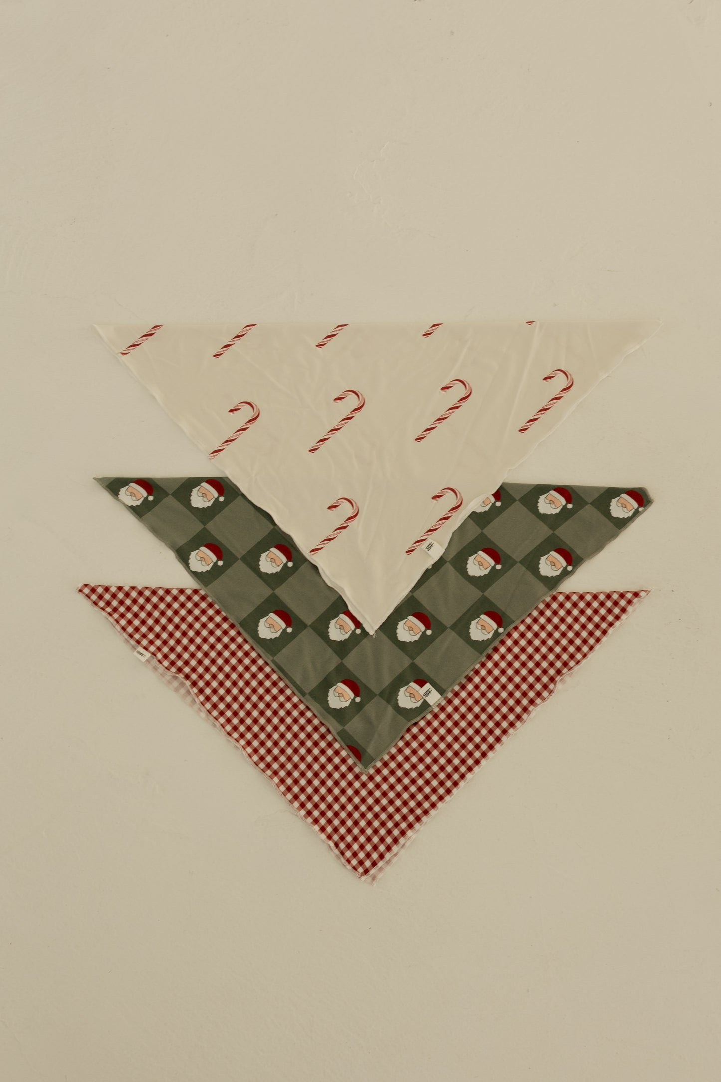 Three triangular Bamboo Bandana | Santa Checkerboard pet bandanas by forever french baby on a light background: white with candy canes on top, green plaid with Santas in the middle, and red gingham at the bottom, all in soft bamboo viscose.