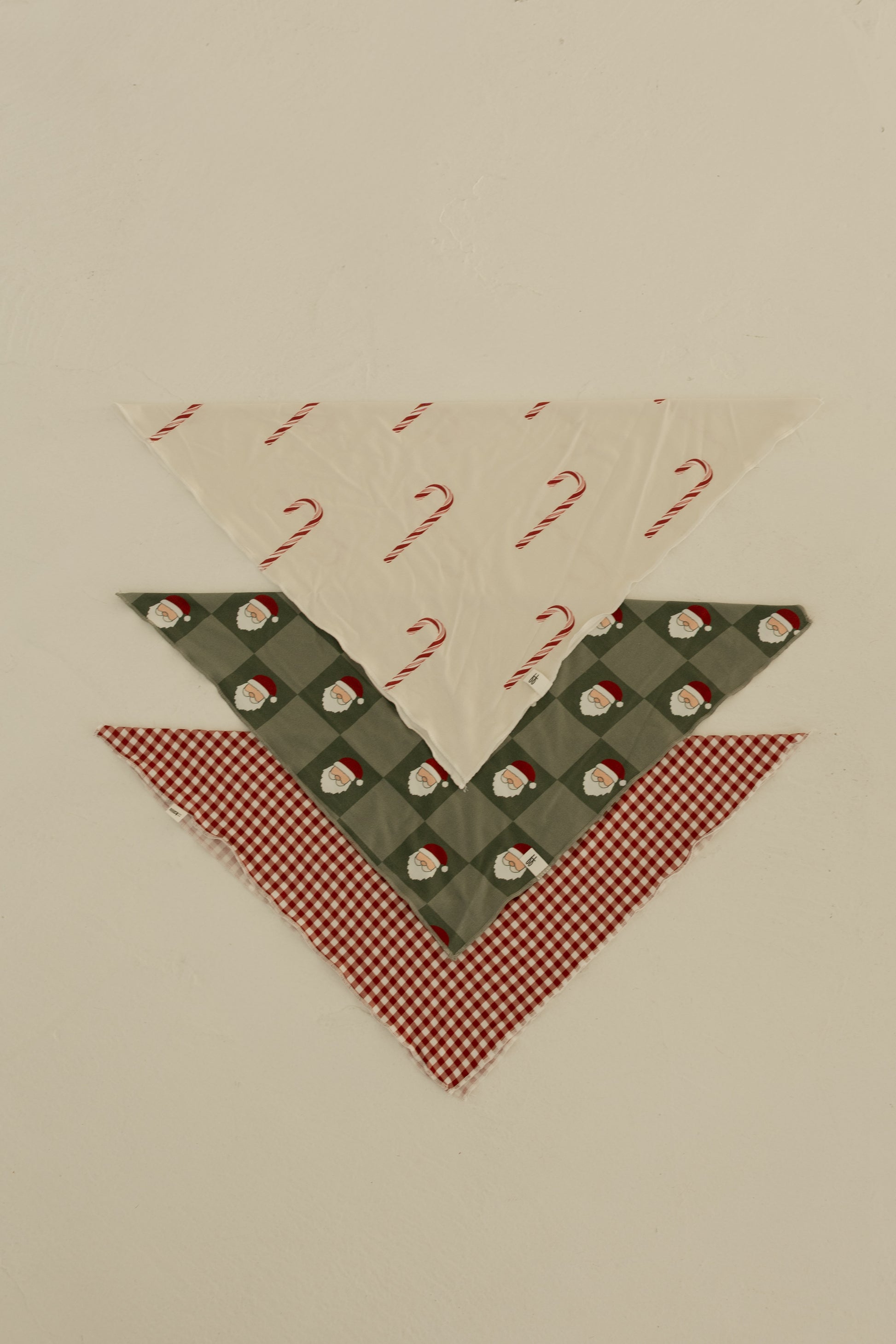 Three Bamboo Bandanas by forever french baby are stacked: candy cane print on top, Santa faces on green plaid in the middle, and red and white gingham on the bottom—perfect for a festive look!.