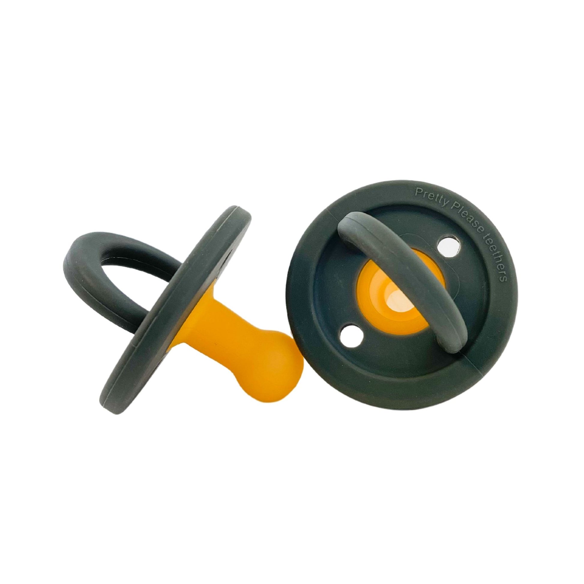 Two Modern Pacifier | Moss by forever french baby are shown lying on a white background, with one facing up and the other facing down. They have dark green rims and yellow nipples and handles, showcasing a silicone design that ensures durability.