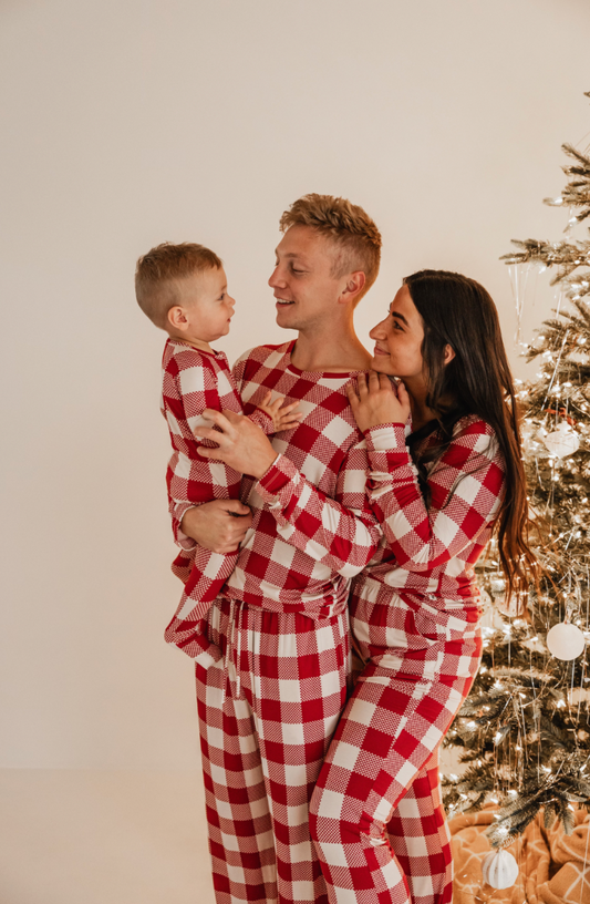 A family of three, wearing forever french baby’s Classic Christmas Men Bamboo Pajamas, stands by a beautifully decorated tree. The parents smile at their young child, held by the father, in the warmly lit room, evoking a serene holiday atmosphere.