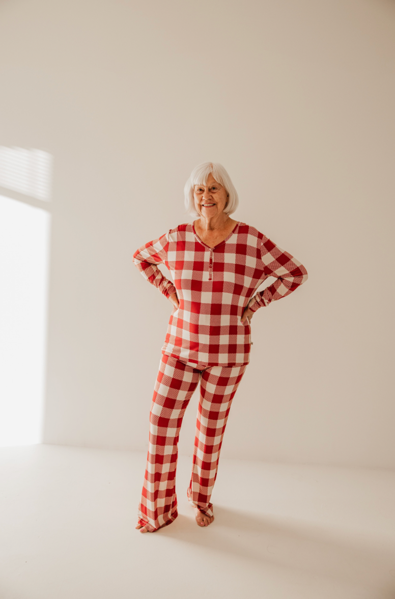 An elderly person with white hair smiles warmly, posing in cozy, Classic Christmas Women Bamboo Pajamas from forever french baby. The brightly lit room and plain white background provide a simple yet charming backdrop for this delightful moment.