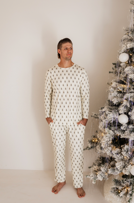 Someone wearing Vintage Christmas Deck the Halls Checkerboard Men Bamboo Pajamas by forever french baby stands near a decorated, snow-dusted Christmas tree with white and gold ornaments in a clean, minimalist space creating a cozy festive atmosphere.