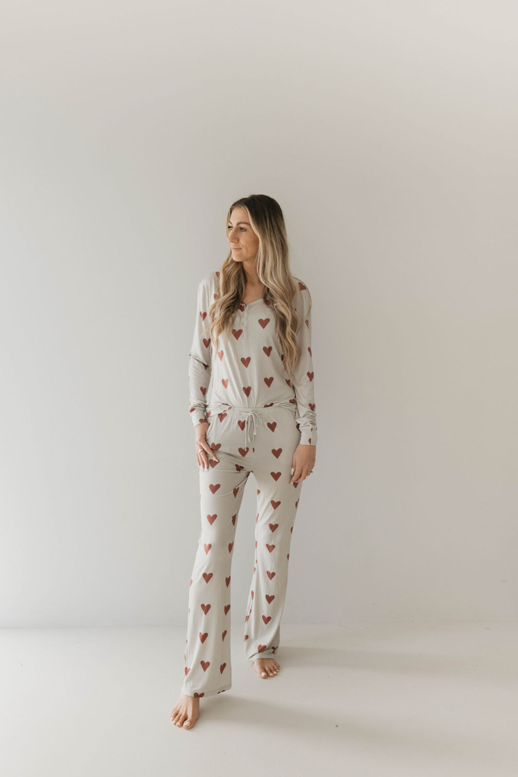 A person with long hair stands barefoot against a plain white background. They are wearing Women's Bamboo Pajamas by forever french baby, featuring long sleeves and pants adorned with Queen Of Hearts Paisley’s Hand Drawn Print. Their relaxed and casual posture adds to the comfort of the cozy attire.