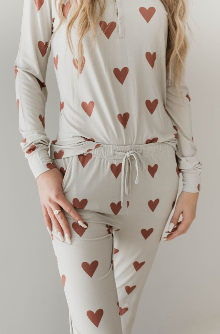 A person wearing the Women's Bamboo Pajamas from forever french baby, featuring a Queen of Hearts paisley hand-drawn print. The pajama top has long sleeves, and the pants have a drawstring waist. The person has long, wavy blonde hair, and their left hand is resting in the pocket of the pants.