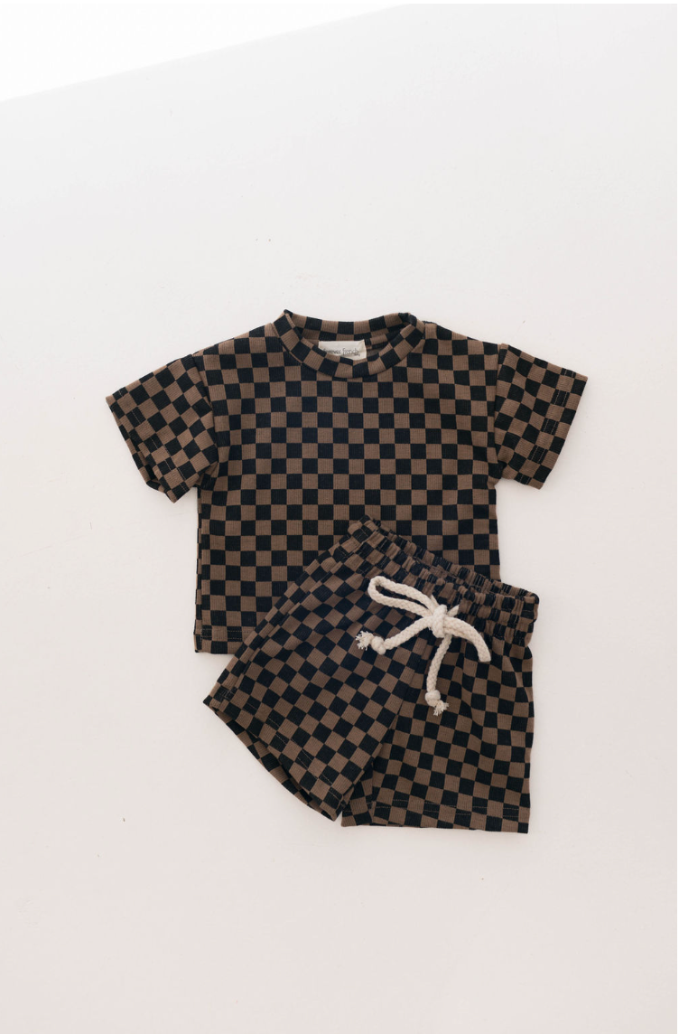 Introducing the Ribbed Short Set | Black & Brown Checkerboard by forever french baby: a coordinated children's outfit for ages 0-9 years, including a short-sleeved shirt and shorts. The ensemble showcases a stylish Black & Brown Ribbed Checkerboard pattern. The shorts feature an elastic waistband with a drawstring tie, all beautifully presented against a plain white background.