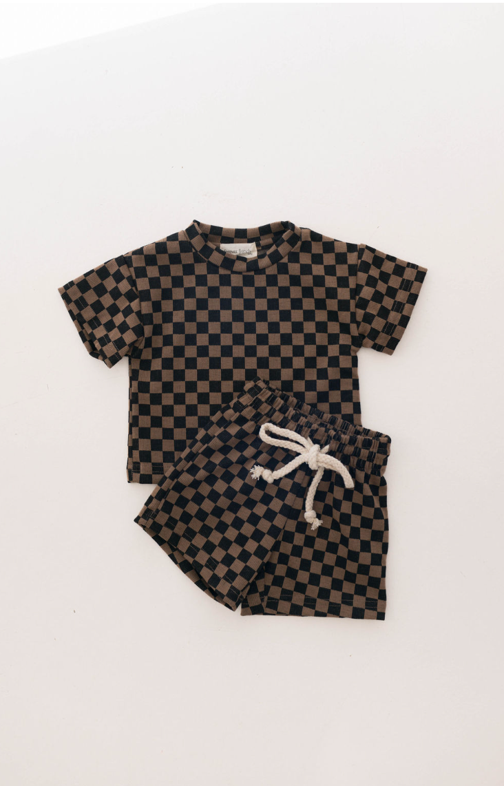 The "Ribbed Short Set | Black & Brown Checkerboard" by forever french baby is an effortlessly stylish children's outfit suitable for ages 0-9 years. It includes a short-sleeved t-shirt and shorts, both adorned with a Black & Brown Ribbed Checkerboard pattern. The shorts feature a white drawstring at the waist. Laid flat on a plain white background, this set exudes casual chic.