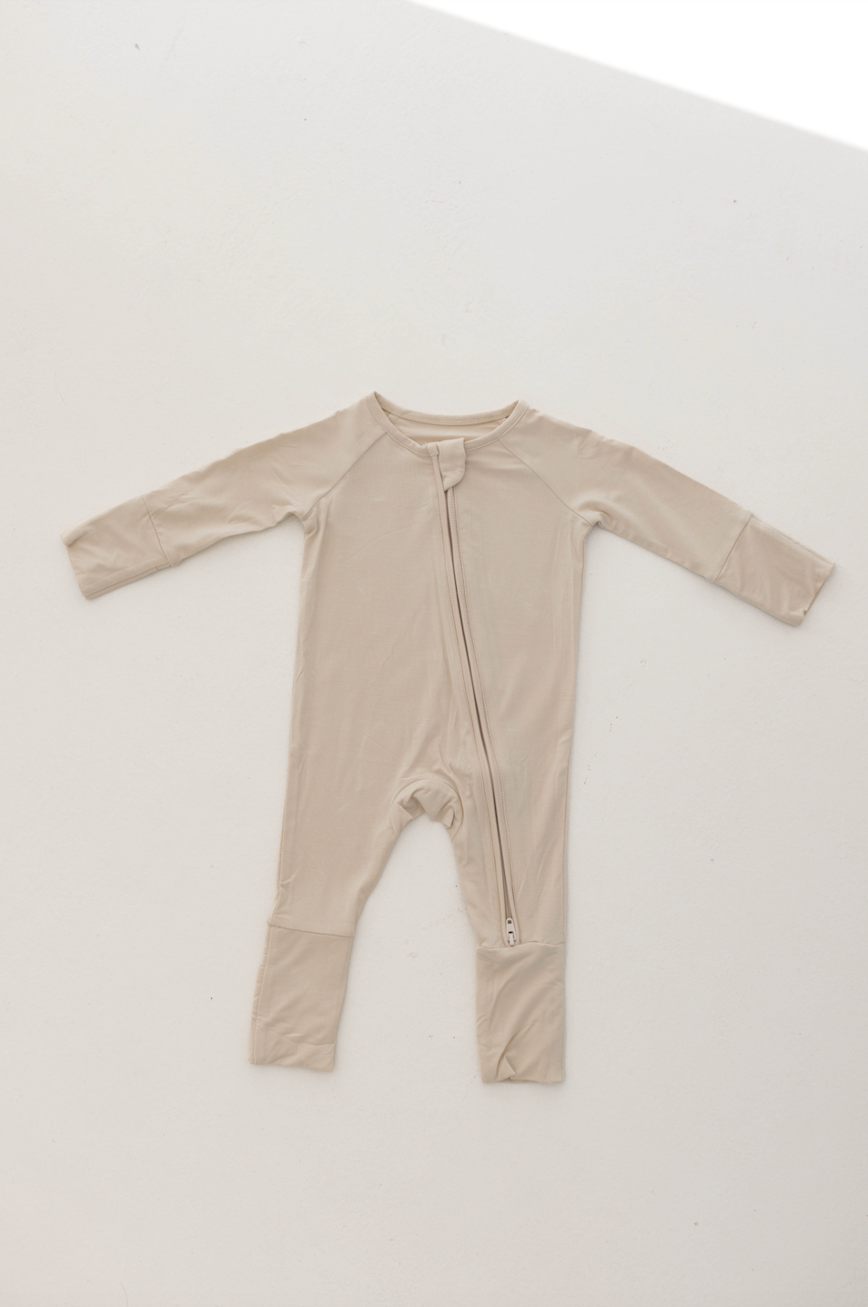 The Bone-colored Bamboo Zip Pajamas from forever french baby showcase a hypo-allergenic design, featuring a diagonal zipper running from the left shoulder to the right leg. This long-sleeved garment with folded cuffs at the legs provides both comfort and warmth. The onesie is displayed laid flat on a white surface.