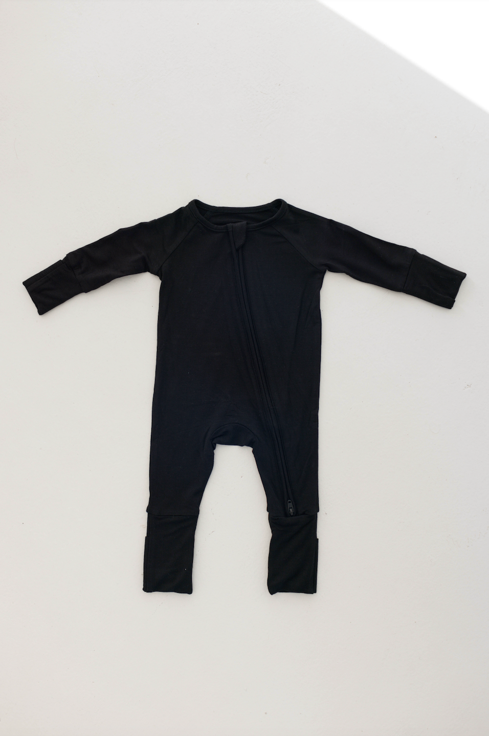 The Bamboo Zip Pajamas in Midnight Black by forever french baby, featuring a zipper down the front and fold-over cuffs on the sleeves and legs, are laid flat on a white background.