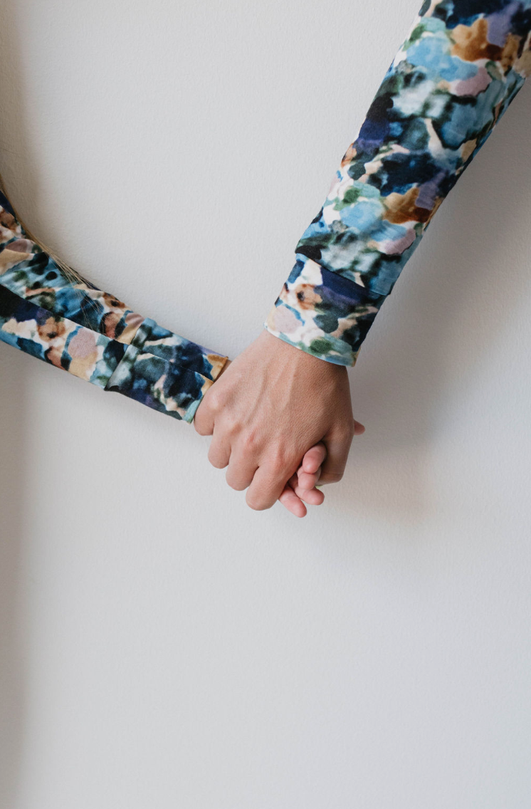 Two people, wearing long-sleeved, multicolored, patterned Bamboo Two Piece Pajamas in the Charli Print by forever french baby, are holding hands against a plain white background. Their clasped hands are centered in the image, emphasizing a sense of connection and unity—an apt symbol for autism awareness.