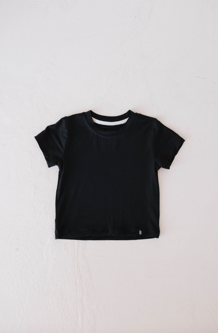 A Basic Bamboo Tee in Midnight Black from forever french baby is laid flat on a light-colored surface. This t-shirt, crafted from soft bamboo fabric, features a round neck and a small rectangular tag at the bottom. The smooth and soft texture of this bamboo t-shirt stands out immediately.