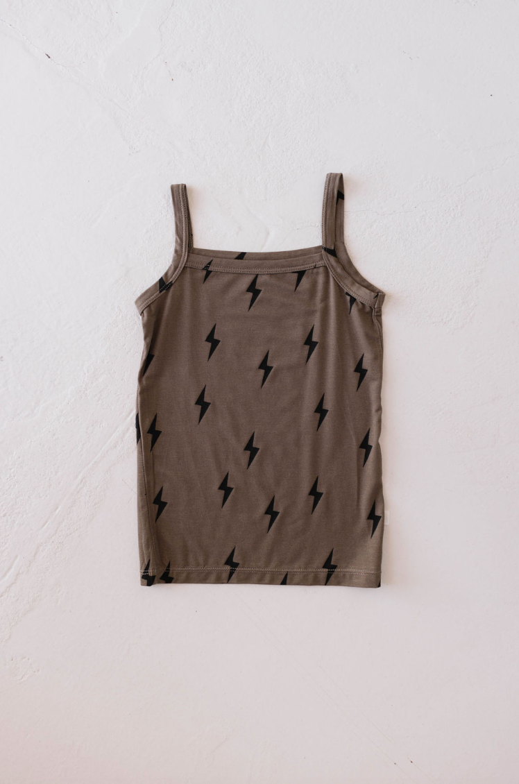 A Basic Bamboo Tank | Lightning Bolt from forever french baby, featuring thin straps and a sleeveless, light brown design made of soft bamboo fabric, lies flat on a white, textured surface. The tank top features a pattern of small black lightning bolts evenly distributed across the fabric for an added touch of flair.