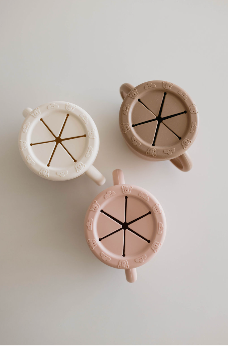 Three BPA-free Snack Cups with Removable Lids from forever french baby in white, brown, and pink are arranged on a light surface. Each silicone cup features adorable bear designs around the rim and ensures easy snacking while keeping the snacks secure.