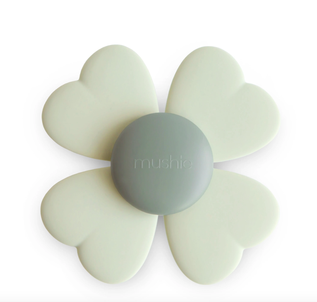 A floral-shaped spinning teether featuring a smooth, light gray center and four heart-shaped petals in a soft cream hue, embossed with the "Mushie" brand name.