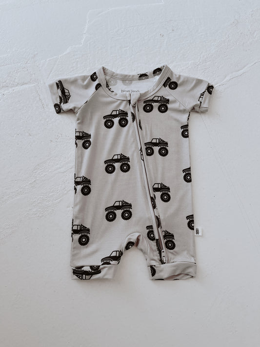 The forever french baby Shortie Bamboo Zip | Monster Truck is a short-sleeved, light gray romper with breathable fabric and black monster trucks, finished with a zipper—perfect for little ones needing comfort and style.