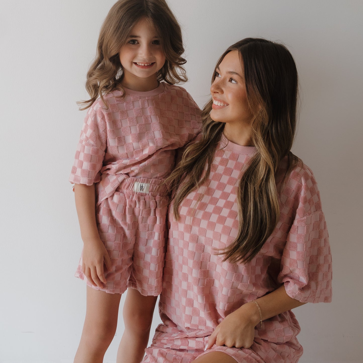 A woman and a young girl smile at each other in matching Women's Terry Short Sets in Sea Pink from forever french baby, standing against a plain white background.