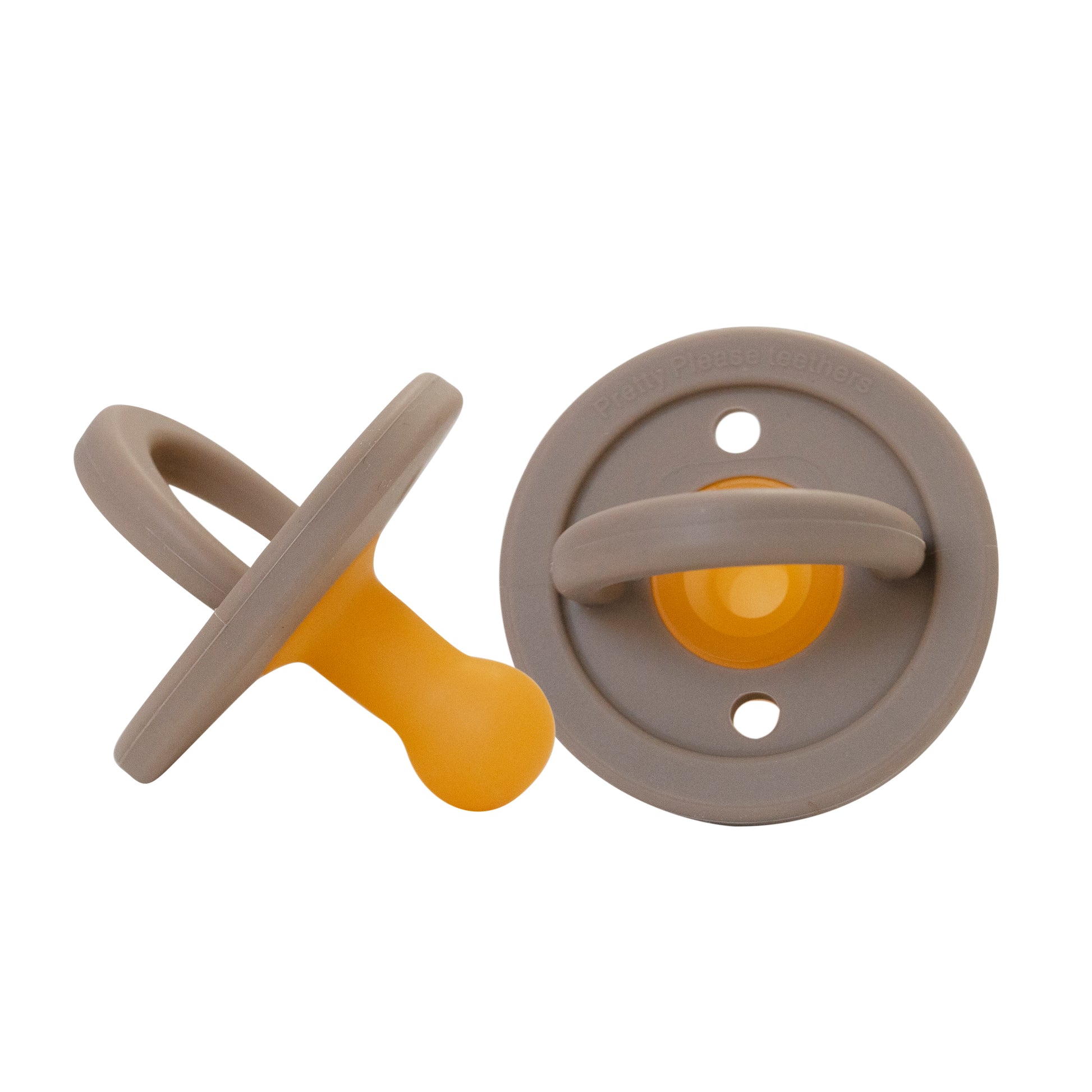 Two BPA-free Modern Pacifier | Warm Taupe from forever french baby feature a sleek silicone design with gray rings and bases, paired with orange nipples. One pacifier lies flat, showcasing the ring side, while the other stands upright to display the nipple side.