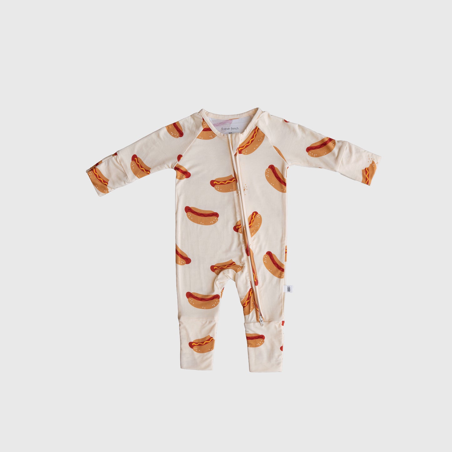 The forever french baby Bamboo Zip Pajamas | Hot Dogs is a cream-colored bamboo viscose baby onesie with a zipper and an all-over hot dog print, shown on a plain light background.