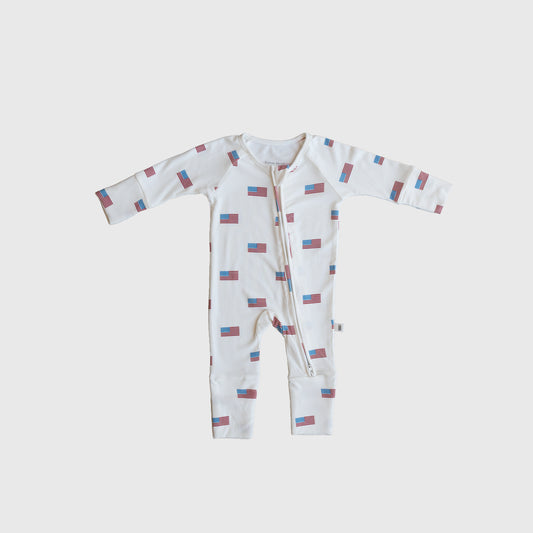 The Bamboo Zip Pajamas | Americana Ribbed by forever french baby is a white hypoallergenic baby onesie with a front zipper and an all-over small American flag pattern, shown flat on a plain white background.