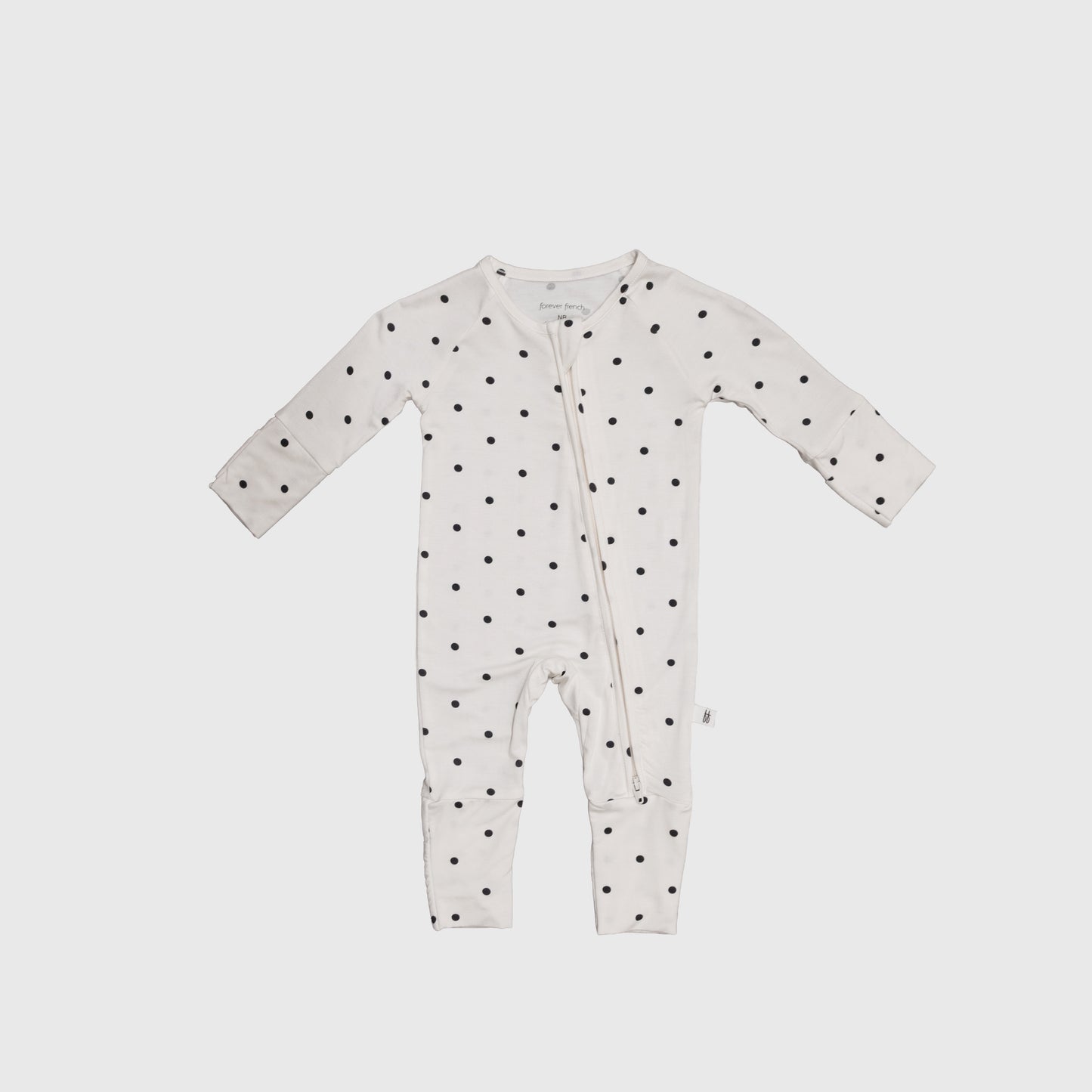 The Bamboo Zip Pajamas | Annie by forever french baby is a white onesie with long sleeves and legs, black polka dots, and an angled zipper, crafted from breathable fabric for all-night comfort.