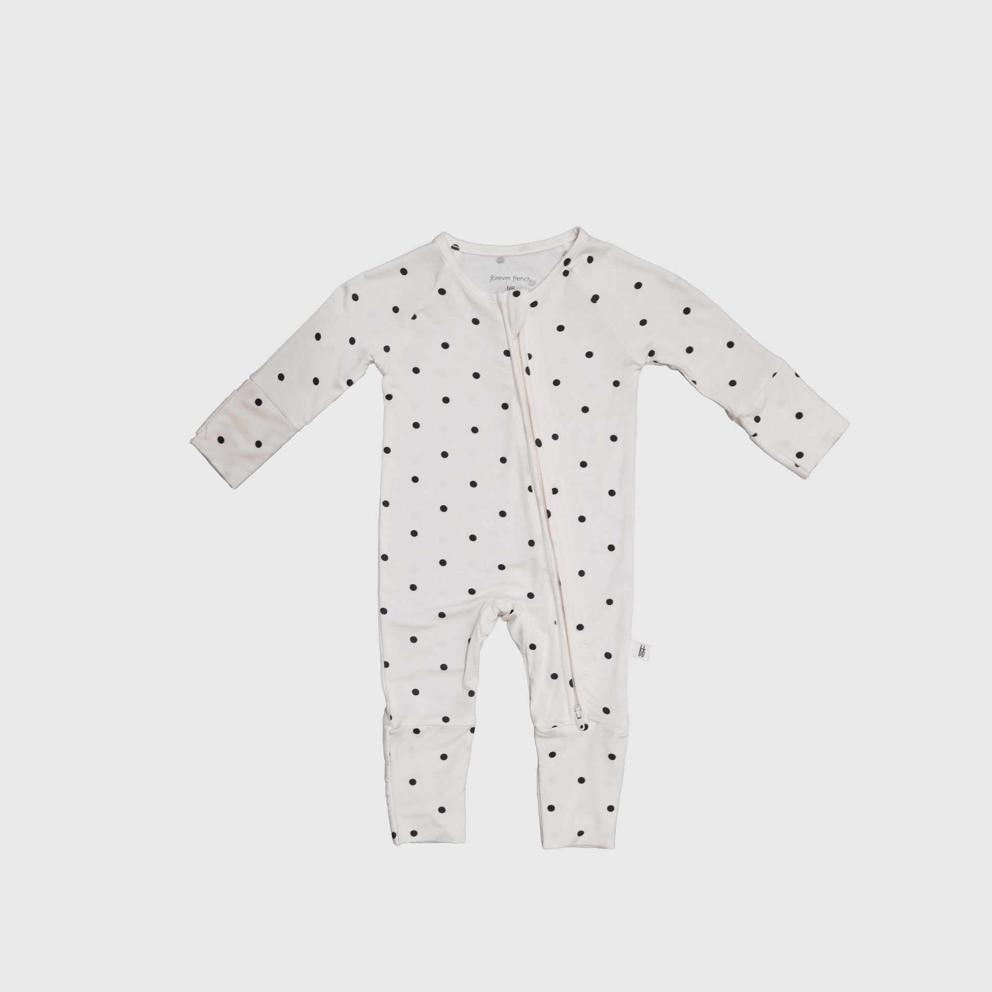 The Bamboo Zip Pajamas | Annie by forever french baby is a white onesie with long sleeves and legs, black polka dots, and an angled zipper, crafted from breathable fabric for all-night comfort.