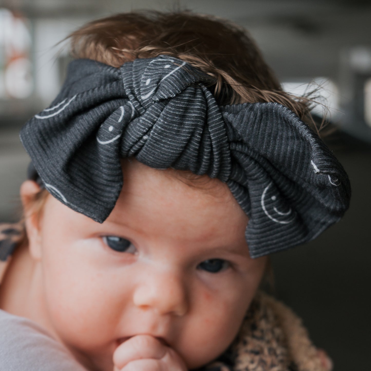 A baby wearing the forever french baby Bamboo Head Wrap | Smiley Ribbed gazes forward, resting its chin on its hand.