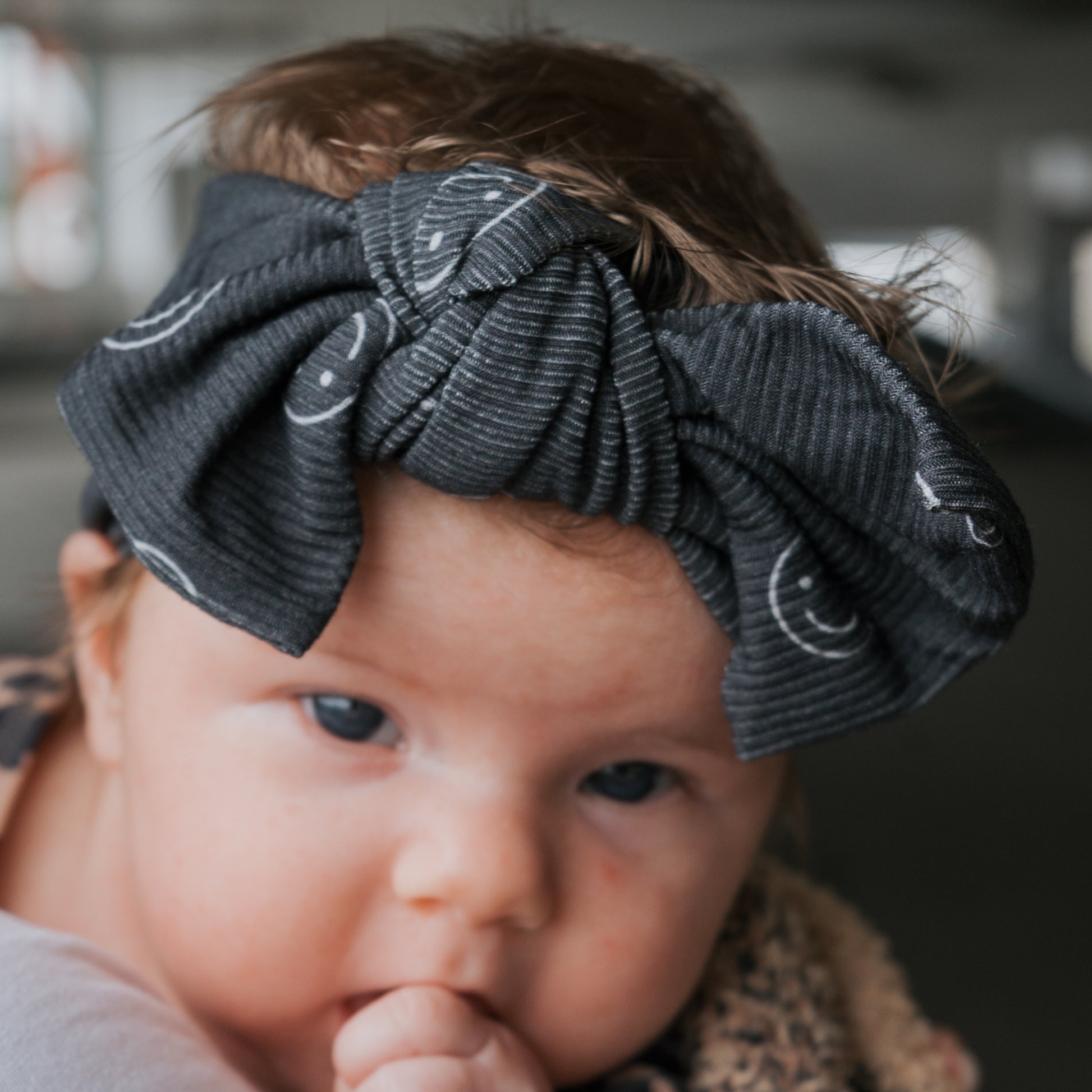 A baby wearing the forever french baby Bamboo Head Wrap | Smiley Ribbed gazes forward, resting its chin on its hand.