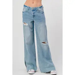 A person is dressed in fashionable High Rise Skater Jeans from I&M JEAN, INC., showcasing their medium wash wide-leg style with ripped details on the front thighs and knees. They complete the look with white sneakers, set against a plain background.