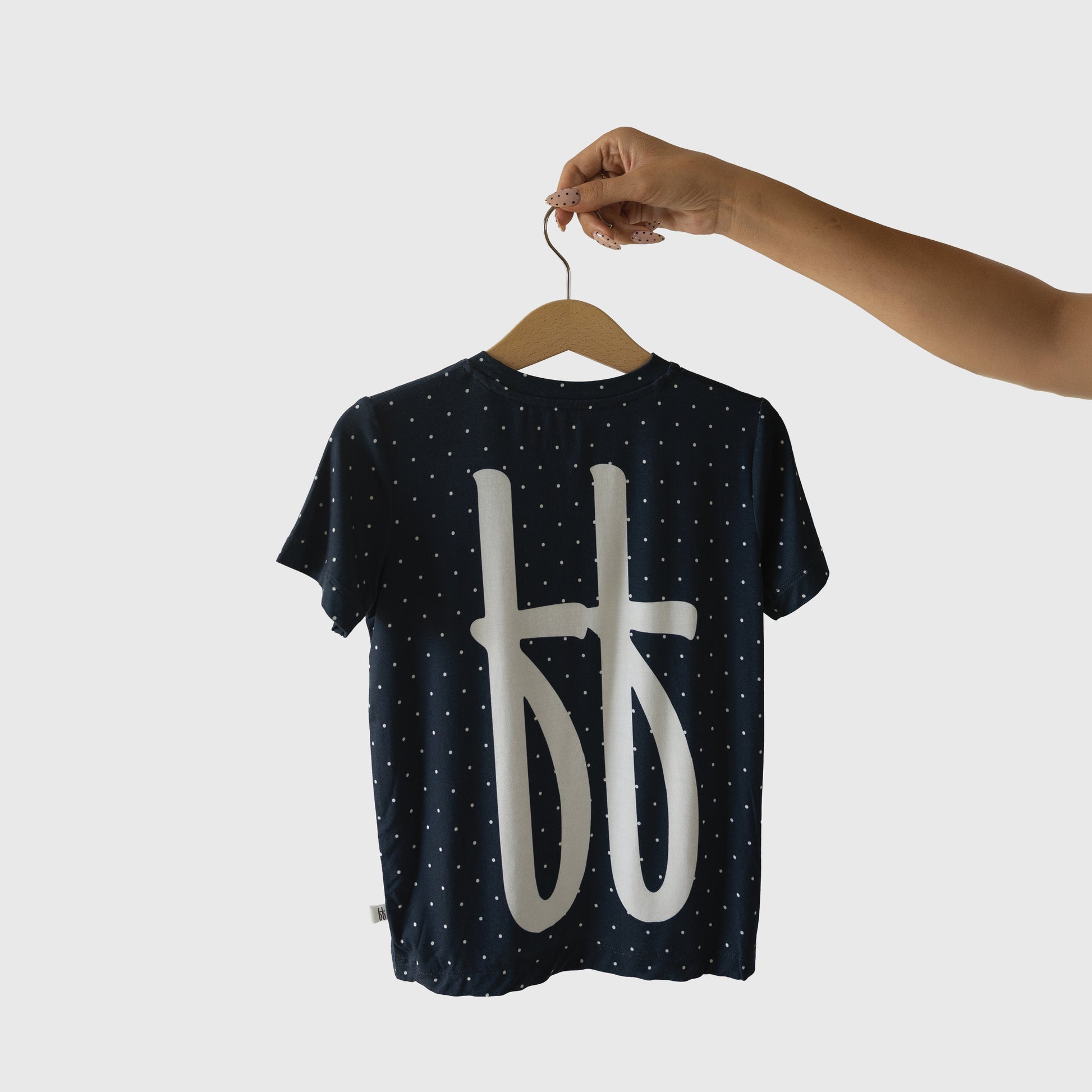 A hand holds the forever french baby Child Short Sleeve Bamboo Lounge Set | Emery—a navy set with small white polka dots and large abstract symbols on the back, perfect for breathable kids’ wear against a plain light background.