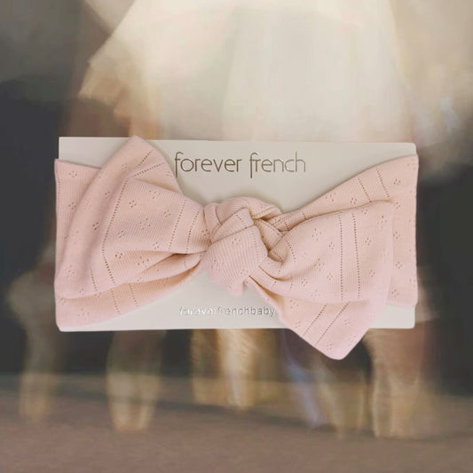 A pale pink, textured Pointelle Head Wrap | Ballerina from forever french baby is displayed on a branded card reading “forever french,” set against a softly blurred cream and brown background. This charming baby head wrap offers both elegance and comfort for your little one.