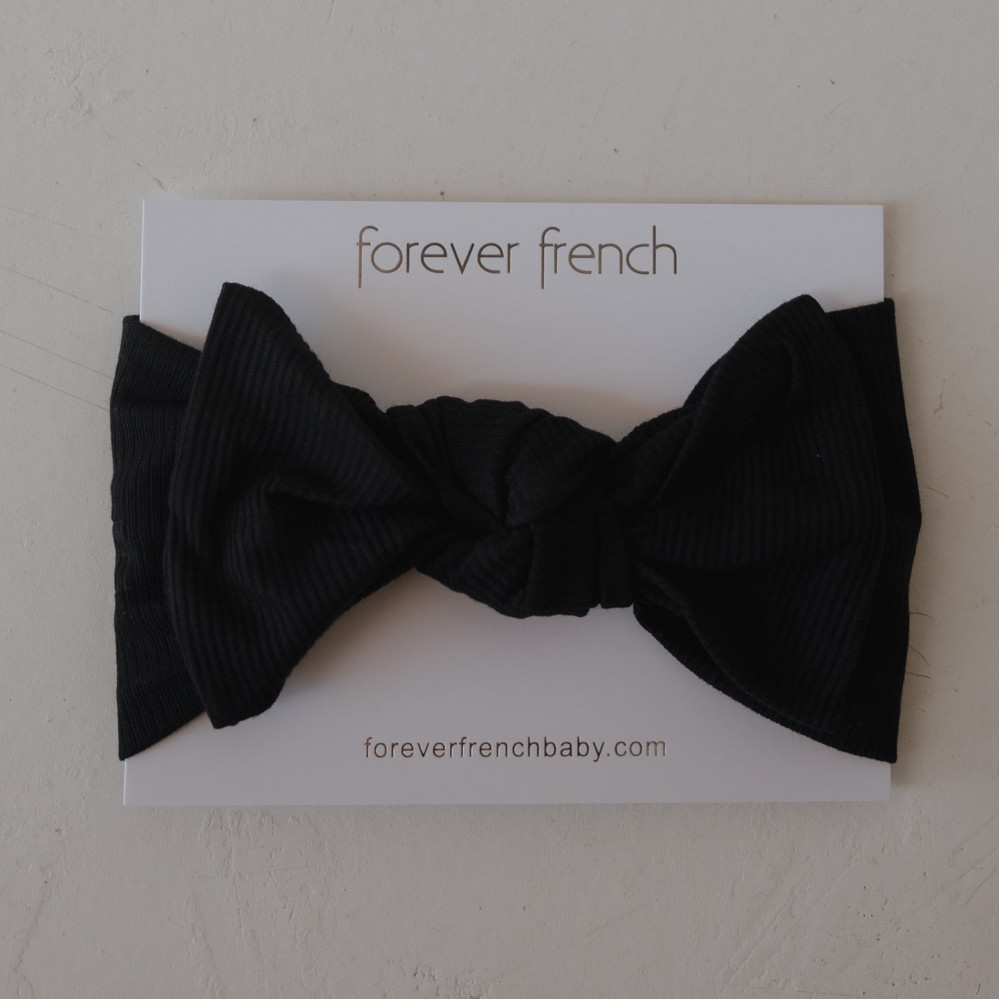 The Bamboo Head Wrap | Ribbed Black by forever french baby is shown on a white card with the brand name and website, making it a stylish accessory for your little one.