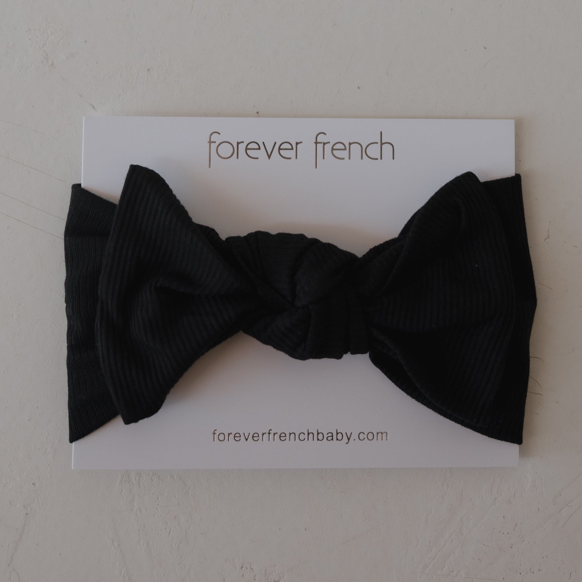 The Bamboo Head Wrap | Ribbed Black by forever french baby is shown on a white card with the brand name and website, making it a stylish accessory for your little one.