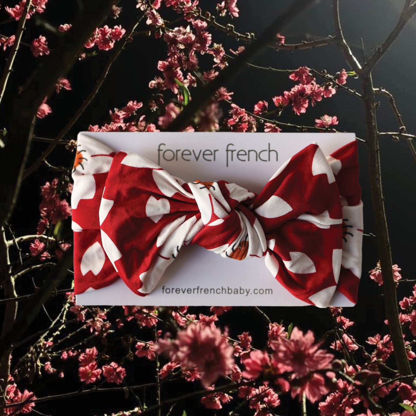 The Bamboo Head Wrap | Cherry Blossoms from forever french baby is displayed against pink cherry blossoms—perfect for your little one.