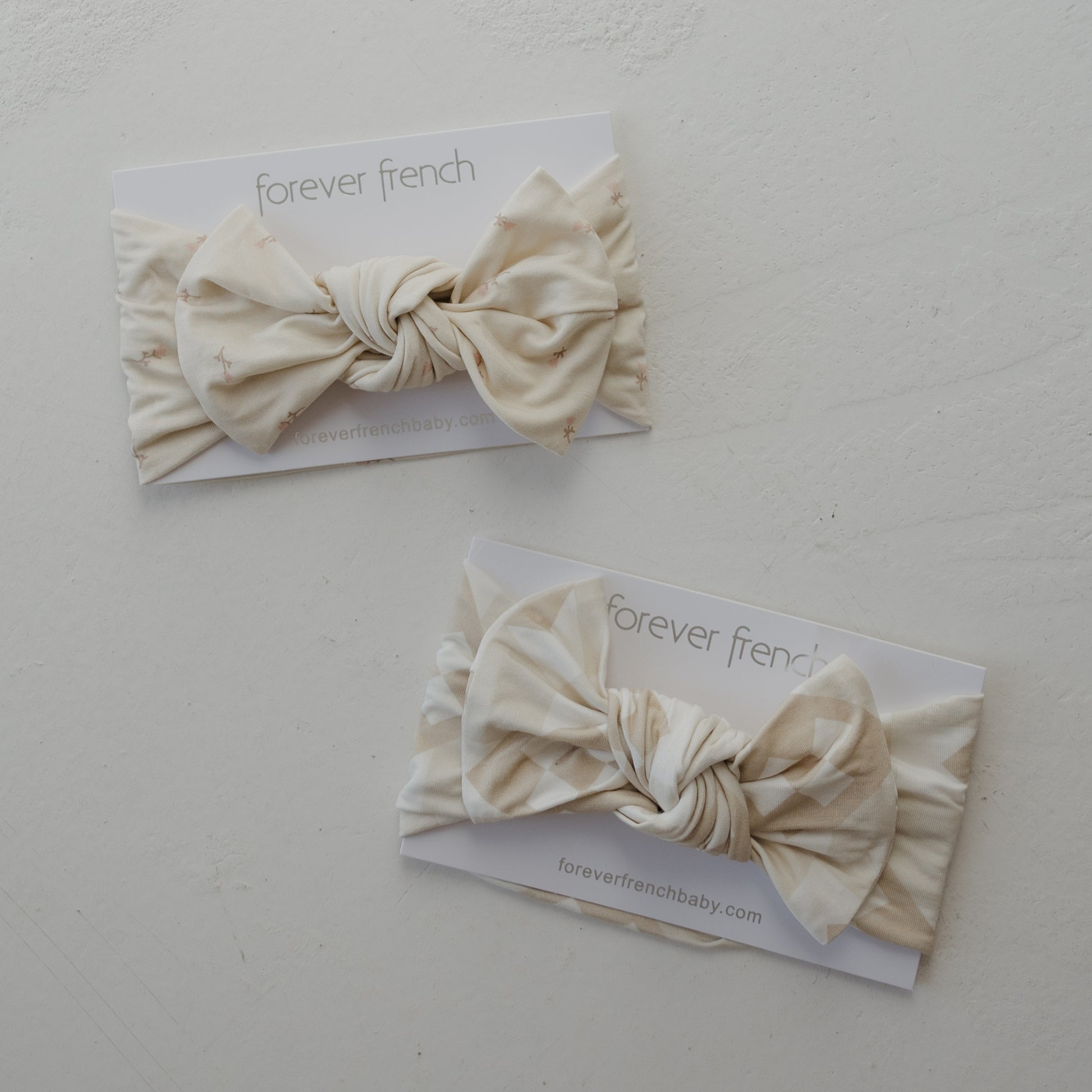 Two cream-colored Bamboo Head Wraps | Lucy from forever french baby, featuring subtle patterns and displayed on branded cards, rest on a white surface—perfect for adding a delicate touch to your little one’s outfit.