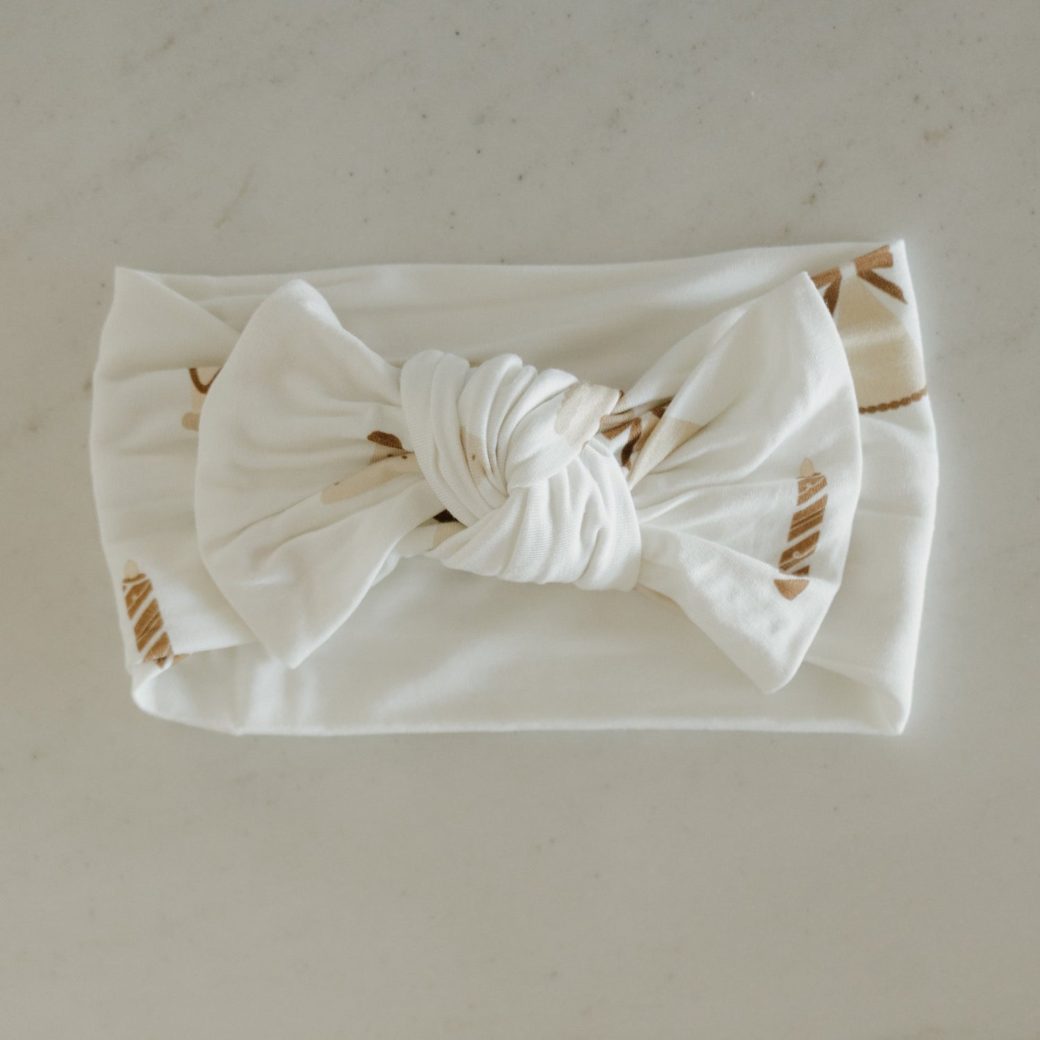 The Bamboo Head Wrap | Birthday Girl by forever french baby is a white fabric baby headband adorned with a large twisted bow in the center and subtle beige leaf patterns, elegantly displayed on a light surface—ideal as an elegant bamboo accessory or as the perfect birthday girl gift.