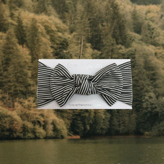 A Bamboo Head Wrap in the Forest Stripe Ribbed pattern by forever french baby, featuring an adjustable bow and displayed on a branded “forever french” card in front of a lake and dense forest backdrop.