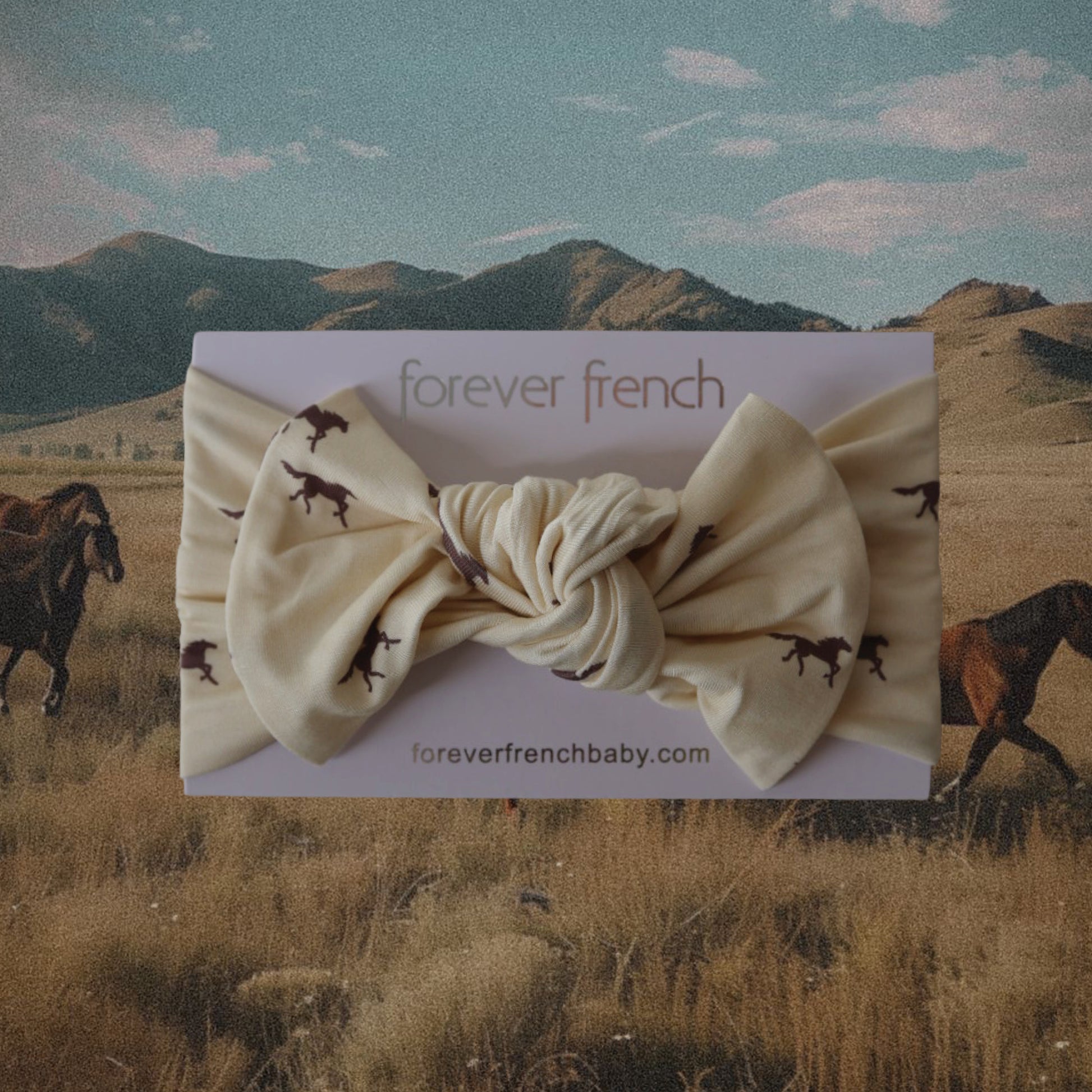 The Bamboo Head Wrap | Wild Horses by forever french baby is shown on a card, featuring horse prints, set against a scenic field with grazing horses and mountains under a blue sky.