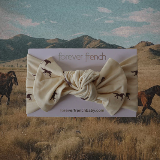 The Bamboo Head Wrap | Wild Horses by forever french baby is shown on a card, featuring horse prints, set against a scenic field with grazing horses and mountains under a blue sky.