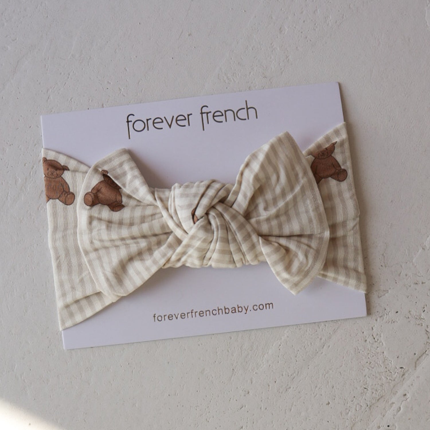 The Bamboo Head Wrap | Teddy by forever french baby features a cream and beige plaid design with small teddy bear prints, shown on branded packaging labeled "forever french baby" and "foreverfrenchbaby.com" on a textured surface.