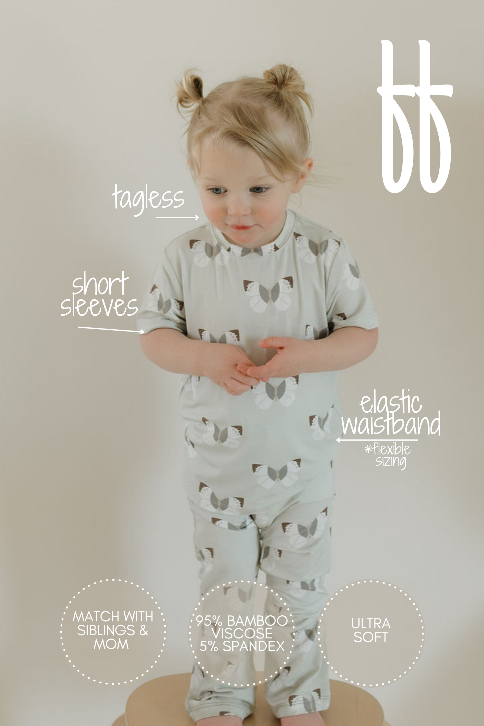 A toddler models the forever french baby short sleeve bamboo lounge set, Butterflies design, against a plain backdrop. These hypoallergenic pajamas are tagless with an elastic waistband and consist of breathable 95% bamboo viscose and 5% spandex for added comfort.