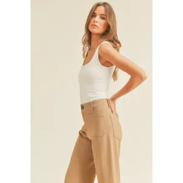 A woman with long brown hair stands against a plain background. She is wearing the Double Layered Square Neck Tank Top in Off White by forever french baby and high-waisted beige pants with her hands in her pockets. She gazes forward with a neutral expression.