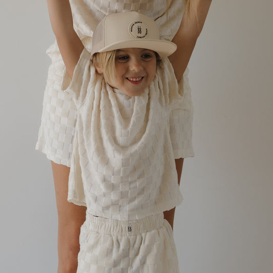 A smiling child in the forever french baby Child Terry Short Set | Coconut Milk is held by an adult in matching outfits, both wearing family matching looks against a plain light background.
