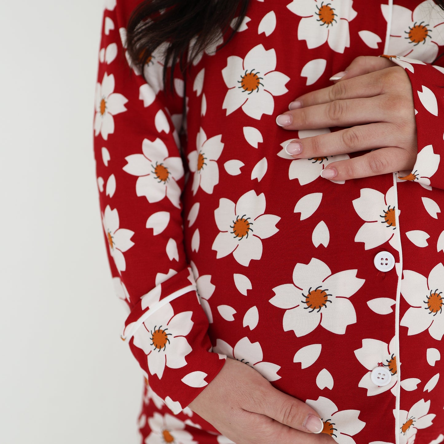 A person wears the forever french baby Women's Bamboo Button Up Lounge Set in Cherry Blossoms and cradles their pregnant belly with both hands against a plain white background.